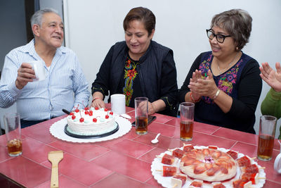 An older man with his friends celebrating a birthday, handing out the cake at an indoor party.