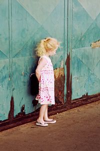 Girl in pink dress standing against weathered wall