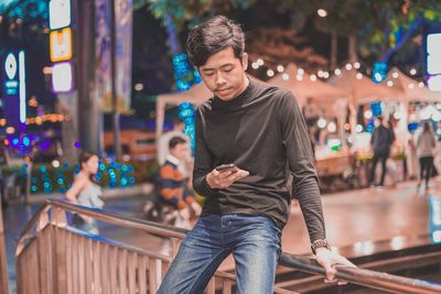 Young man using phone while sitting on railing by staircase 