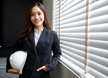 Portrait of young businesswoman standing against window