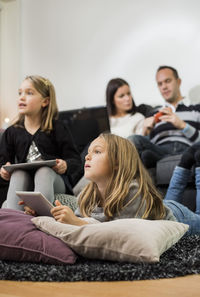 Sisters holding digital tablets with parents in background at home