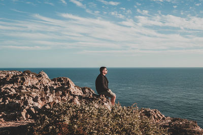 Woman on rock by sea against sky