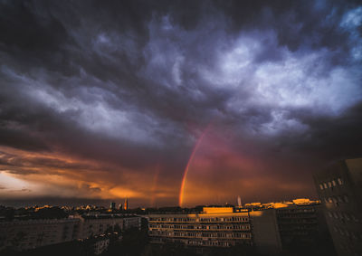 Rainbow over city buildings against dramatic sky