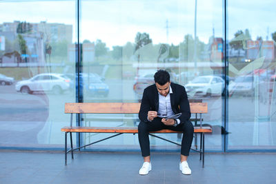 Full length of young man sitting on glass window