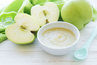 Bowl with baby food and apples on table