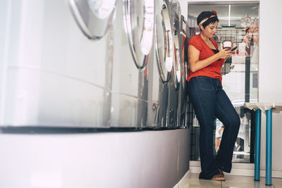 Woman using mobile phone while standing at laundromat