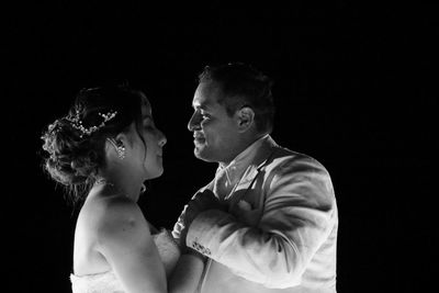 Newlywed couple dancing against black background