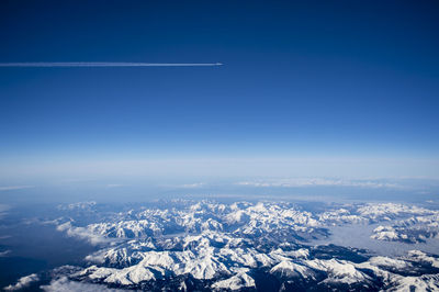 Aerial view of snow covered mountains with airplane flying against blue sky