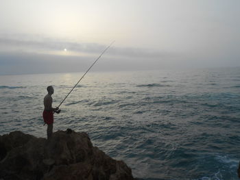 Man fishing in sea against sky