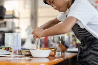 Happy boy cracking an egg for baking a cake in kitchen