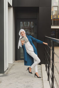 Full length portrait of smiling young woman standing in corridor