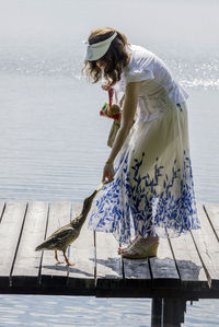 Side view of woman feeding duck while standing on pier at lake