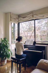 Rear view of woman playing piano at home