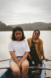 Portrait of females sitting in rowboat at lake against sky