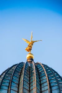 Low angle view of sculpture against building against clear blue sky