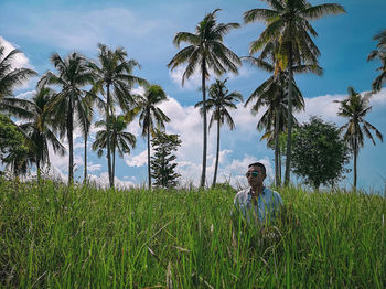Man in sunglasses standing amidst grass against palm trees