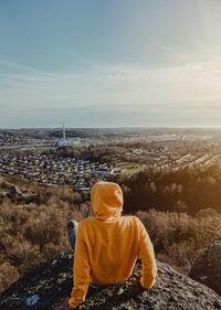 Rear view of man sitting on rock against cityscape