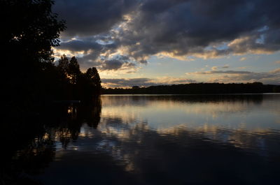 Silhouette of trees by lake against cloudy sky