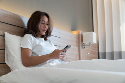 Woman using mobile phone while sitting on bed