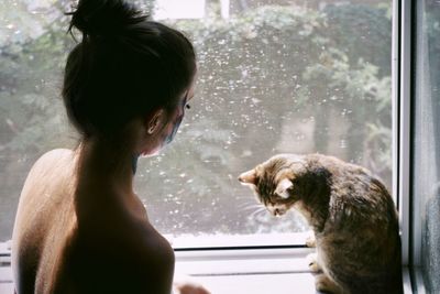 Shirtless woman with cat at window sill