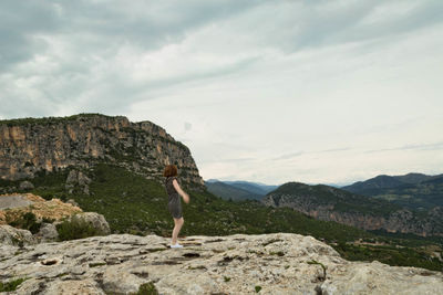 Full length of woman standing on cliff against mountains