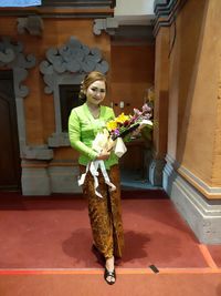 Woman holding flower standing by building