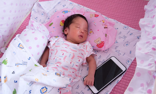 High angle view of baby sleeping by mobile phone in crib