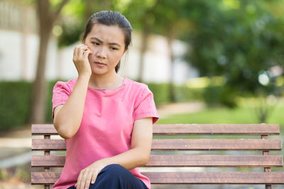 Young woman scratching cheek while sitting on bench at park