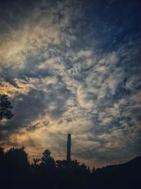 Silhouette of factory against cloudy sky