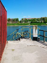 Bicycle parked on steps by river against blue sky