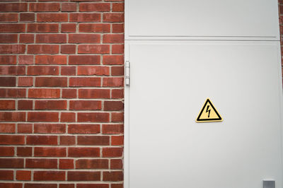 High voltage sign on door by brick wall