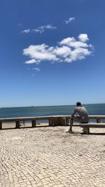Rear view of man sitting on sea against sky