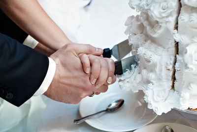 The hands of the newlyweds cut the wedding cake with a knife