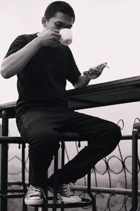 Full length of man using mobile phone while sitting on railing