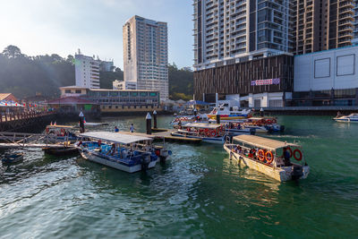 Boats moored in river by buildings against sky in city