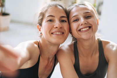 Young fit women friends practice yoga taking selfie on mobile phone in yoga studio