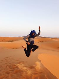 Woman jumping in desert against clear sky