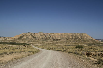 Road amidst desert against clear blue sky