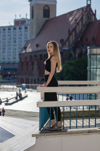 Thoughtful young woman standing on balcony against buildings in city