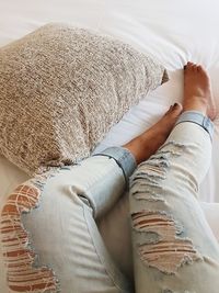 Low section of woman wearing torn jeans while lying on bed at home