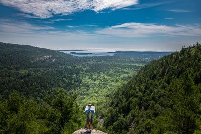 Rear view of mature man looking at landscape while standing on mountain against blue sky