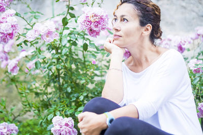 Thoughtful woman with hand on chin sitting by flowering plants in garden
