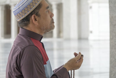 Side view of mature man praying while kneeling at mosque