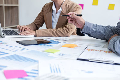 Midsection of two businessmen with graphs on table discussing while using laptop