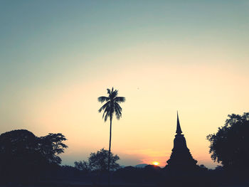 Silhouette coconut and pagoda in temple  against sky during sunset. sukhothai, thailand.