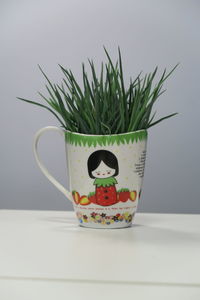 Close-up of grass growing in mug on table against gray background