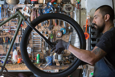 Serious adult man in apron and gloves repairing wheel of bike in modern garage