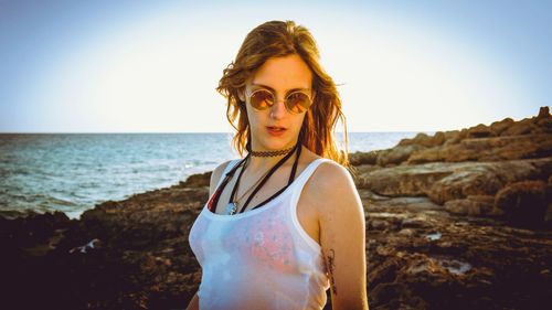 Portrait of young woman standing on rock at beach against clear sky