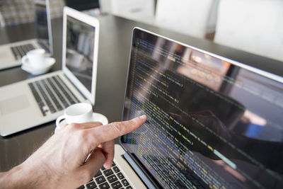 Cropped hand of businessman pointing on laptop in office