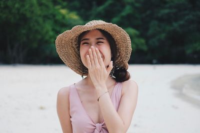 Portrait of happy young woman wearing hat while standing at beach